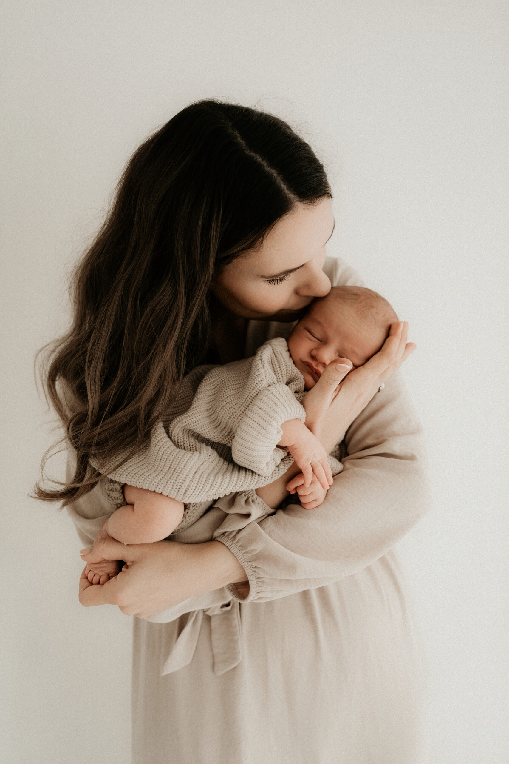 Mutter küsst ihr Neugeborenes liebevoll auf den Kopf