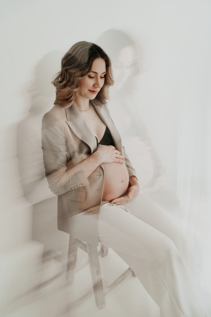 Schwangere Frau im hellen Studio in Lengerich bei Osnabrück und Münster hält liebevoll ihren Babybauch – natürliches und modernes Babybauchshooting.