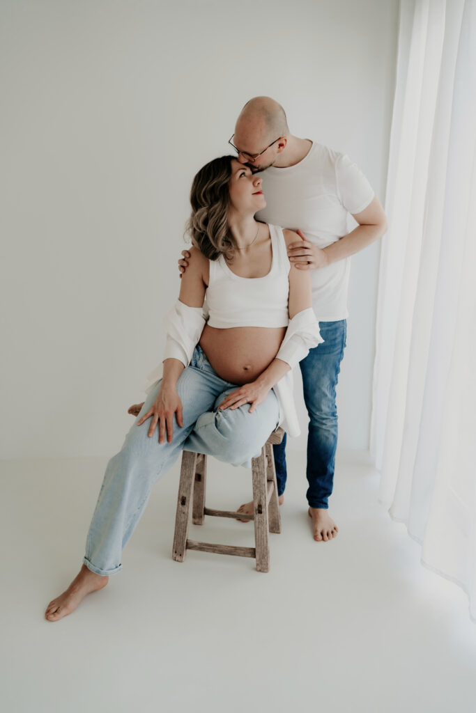 Mann küsst schwangere Frau auf die Stirn im hellen Fotostudio