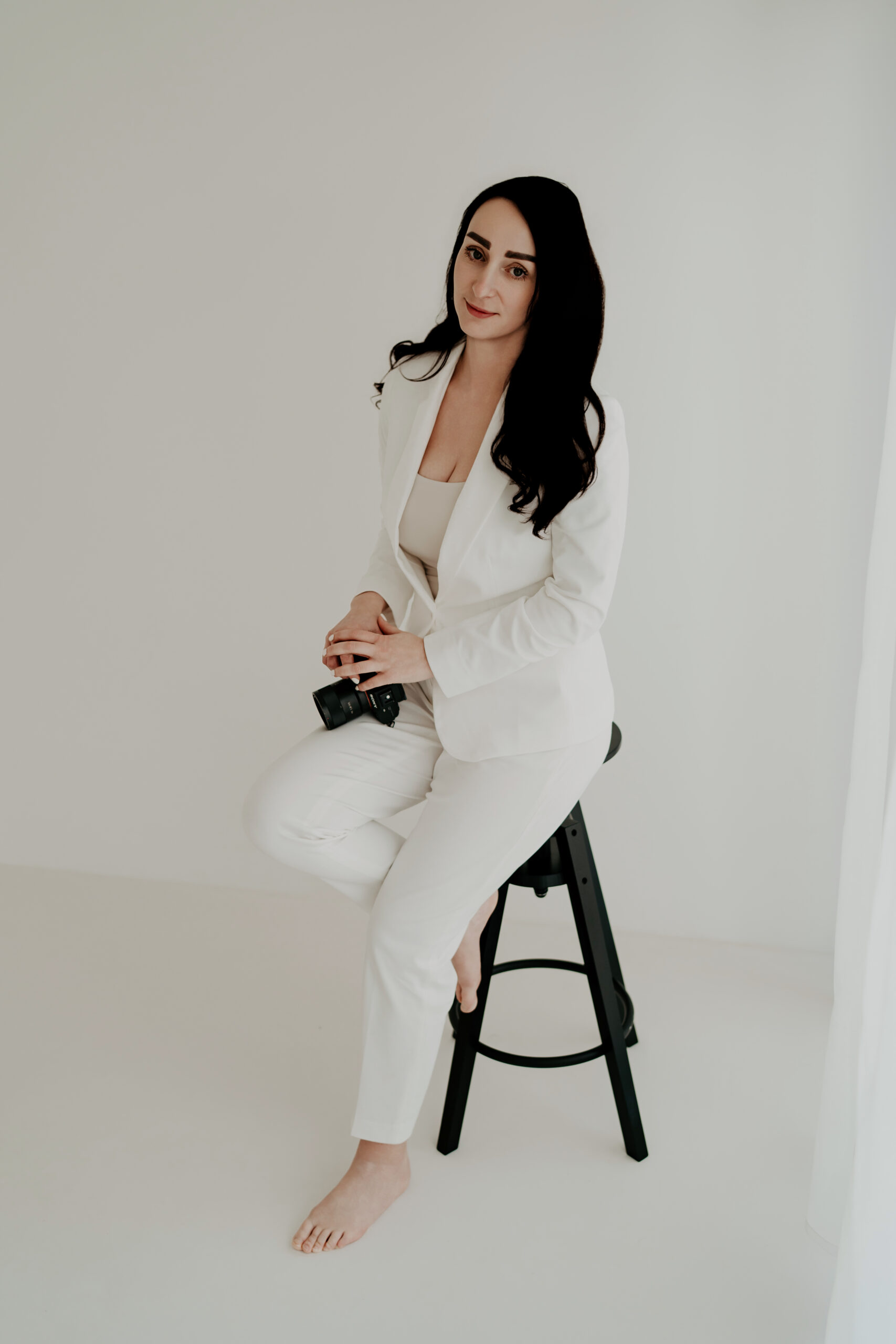 Fotografin Laura Karoline sitzt auf einem Hocker und hält ihre Kamera im Studio.