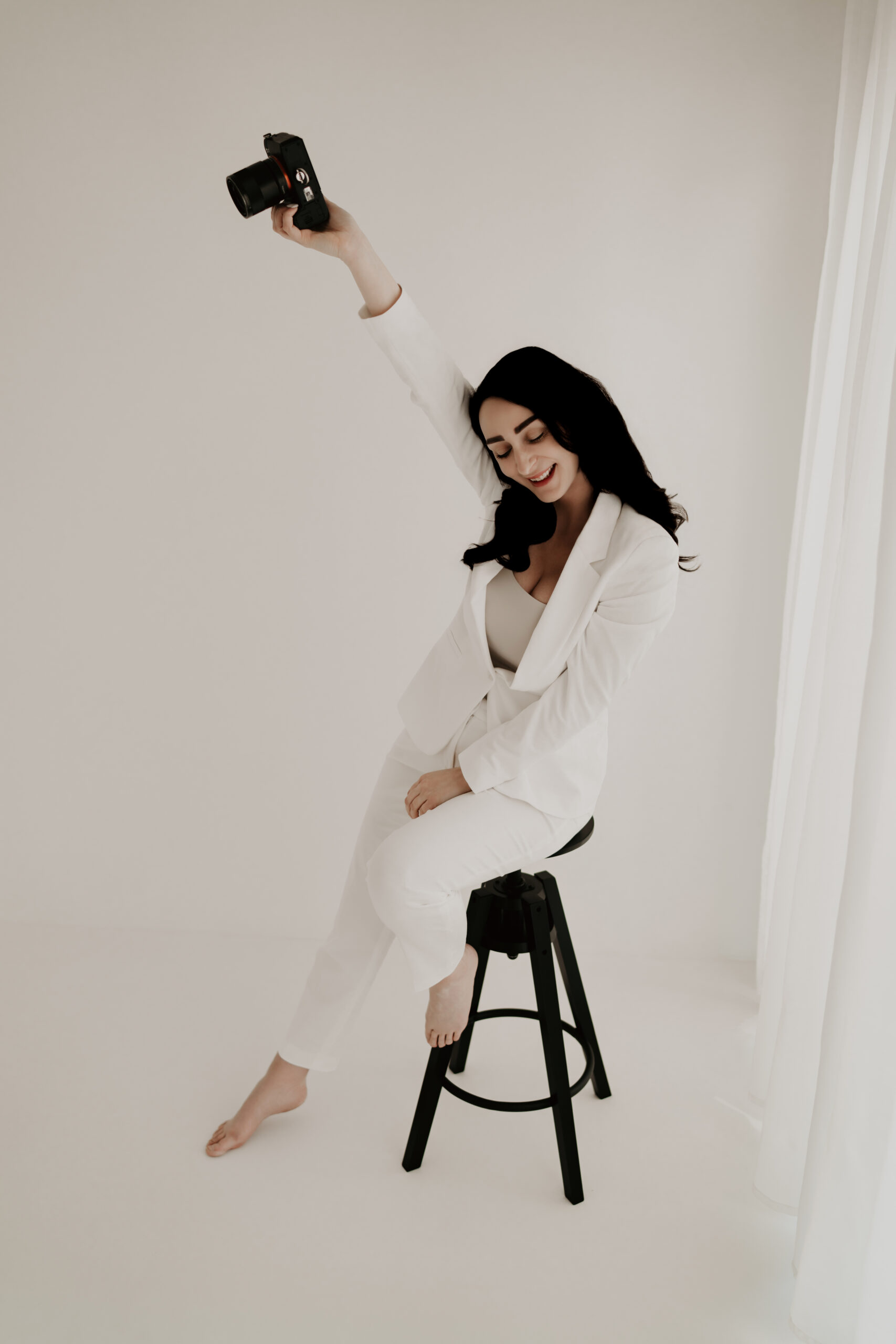 Fotografin Laura Karoline sitzt auf einem Hocker und hält ihre Kamera hoch im hellen Fotostudio.