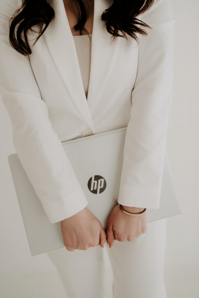 Fotografin Laura Karoline im weißen Anzug hält einen Laptop vor sich im hellen Studio.