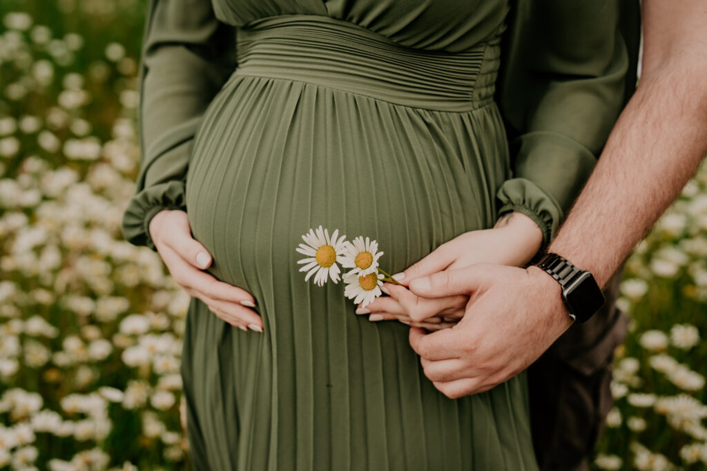 Detailaufnahme eines Babybauchs mit Gänseblümchen während eines Outdoor-Babybauchshootings.