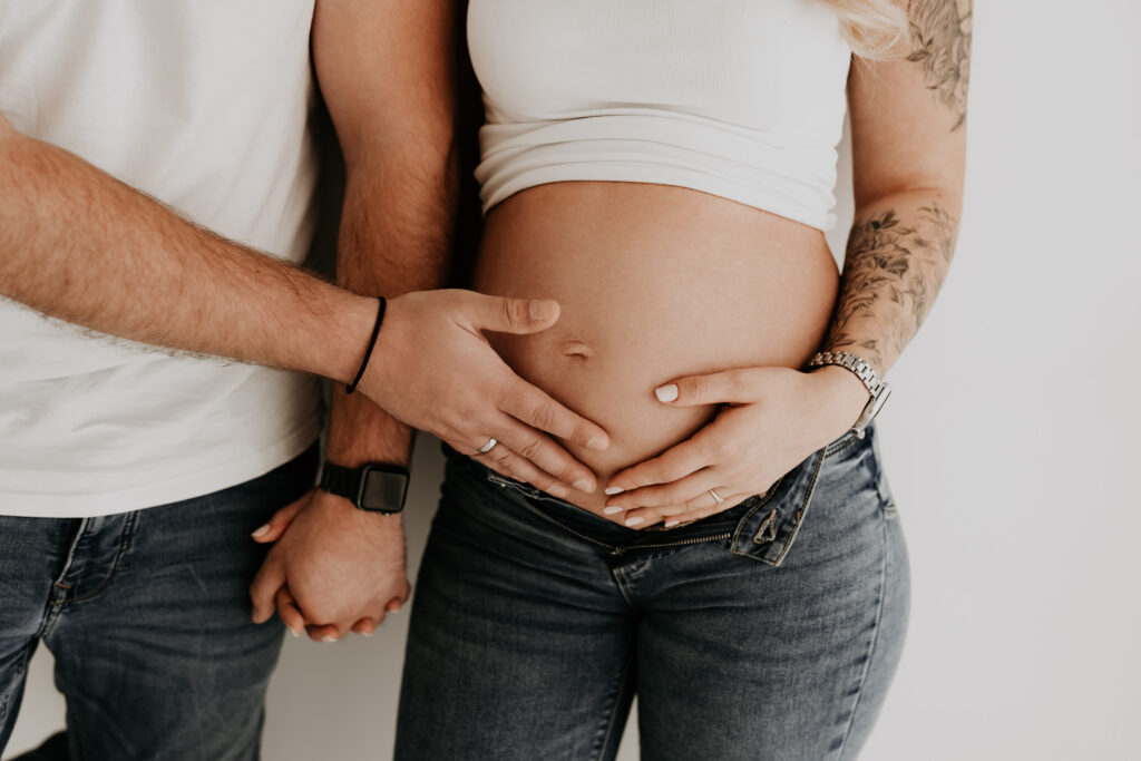 Detailaufnahme der Hände der werdenden Eltern auf dem Babybauch.