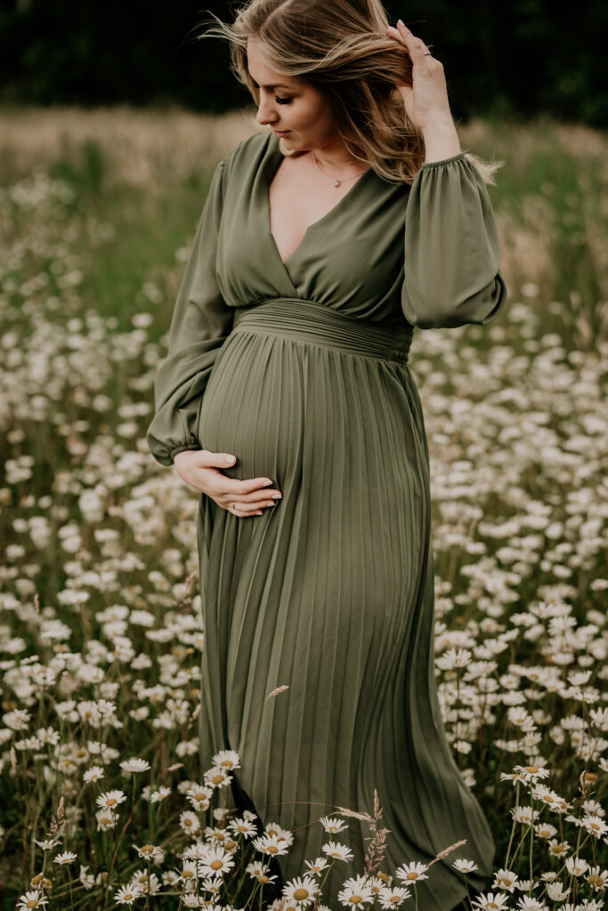 Natürliches Schwangerschaftsporträt einer werdenden Mama im grünen Kleid auf einer Blumenwiese.