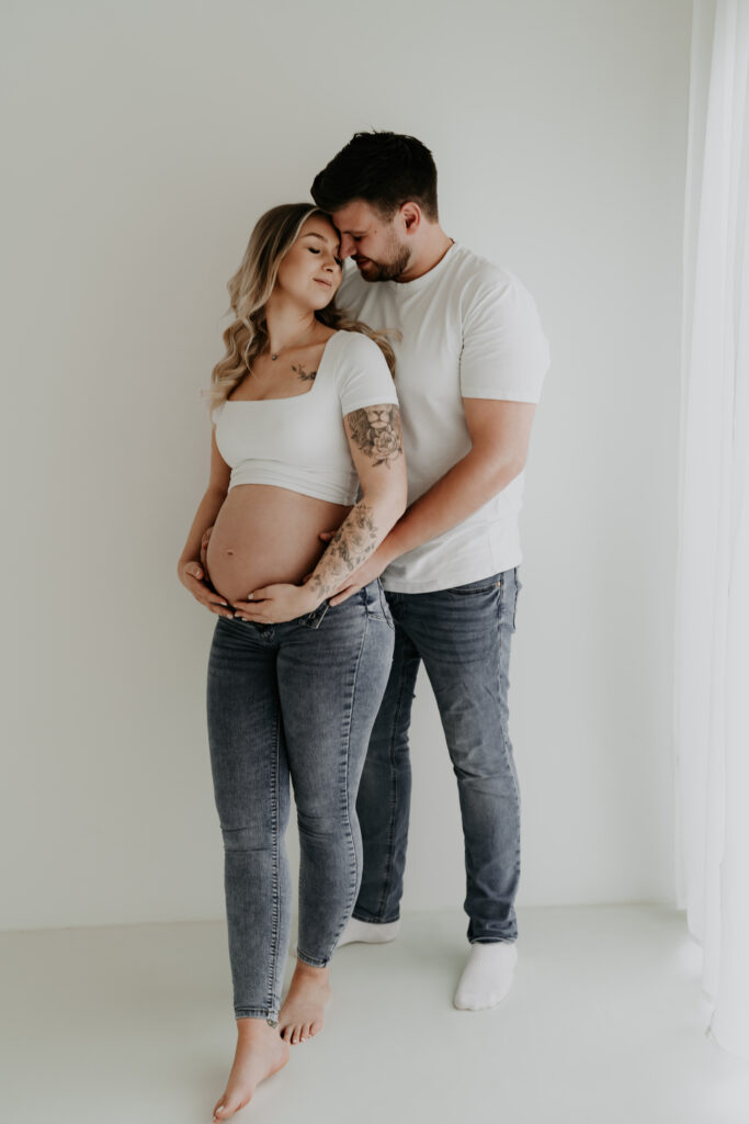 Liebevolle Umarmung eines werdenden Paares beim Babybauchshooting im Studio.