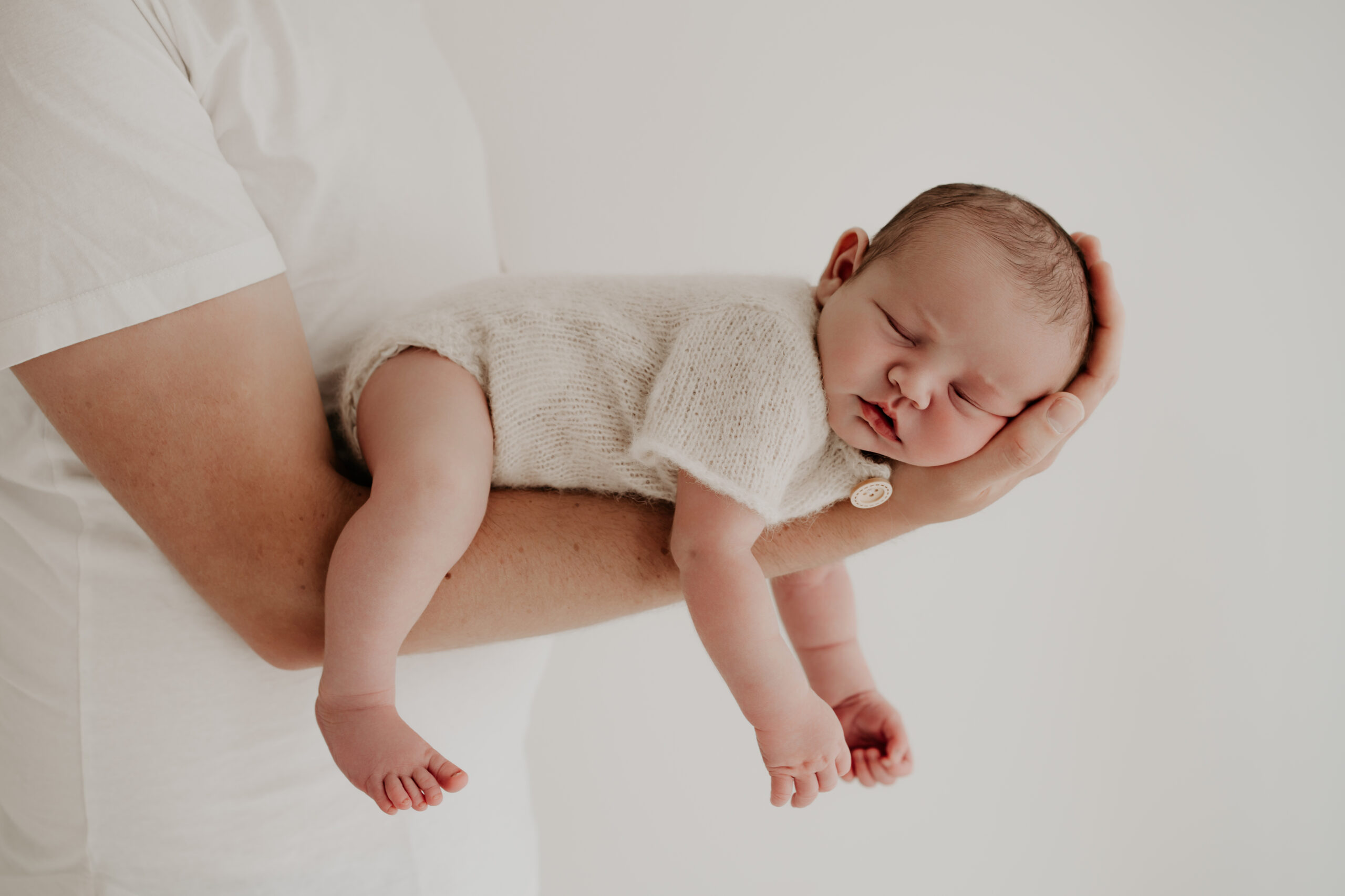Neugeborenes schläft entspannt im Arm seines Papas während eines natürlichen Newbornshootings.