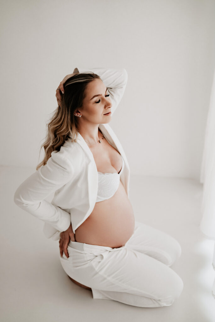 Stilvolle Babybauchaufnahme auf einem weißen Podest im hellen Tageslichtstudio.