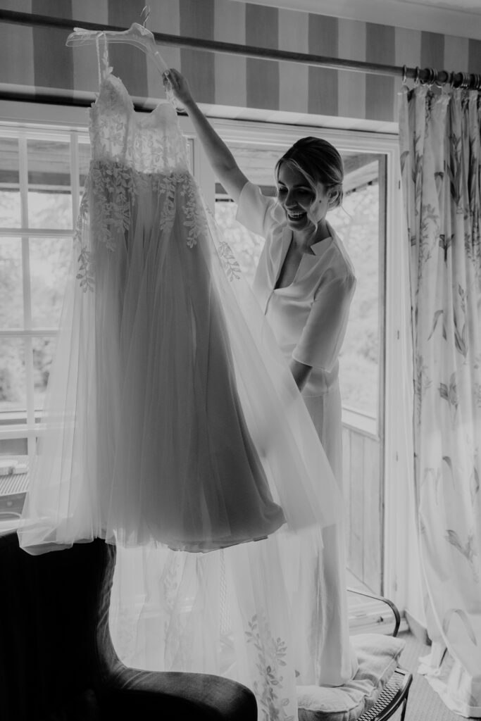 Braut beim Getting Ready mit ihrem Hochzeitskleid am Fenster