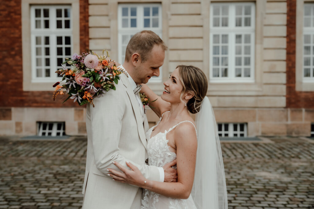 Innige Umarmung des Brautpaares mit farbenfrohem Brautstrauß
